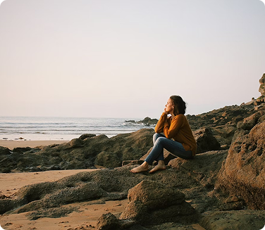 A woman contemplating on some rocks at a beach.