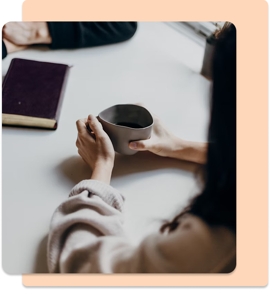 A woman holding a coffee cup and a notebook on a table.